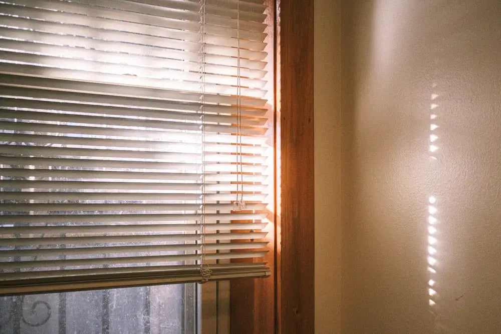 Strong summer sunlight entering a room through closed window blinds