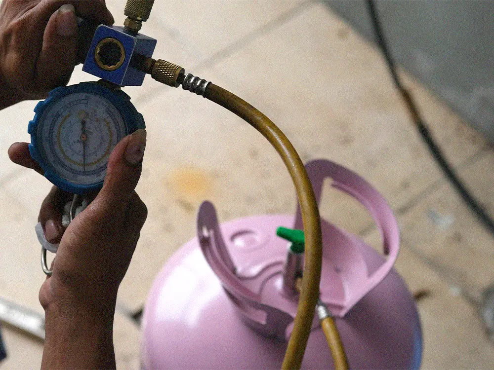 HVAC technician checking pressure gauge while charging R410A refrigerant cylinder